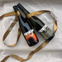 Load image into Gallery viewer, Two wine bottles and two Studio Null glasses with a gold ribbon on a white fabric background