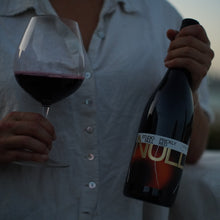 Load image into Gallery viewer, Person holding a bottle and glass of non-alcoholic red wine with a blurred background